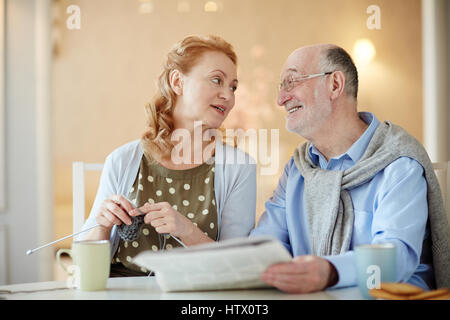 Porträt von älteren Ehepaar, elegante Frau und grauen dunkelhaarigen Mann beisammen sitzen am Küchentisch zu Hause morgen während readin miteinander zu reden Stockfoto