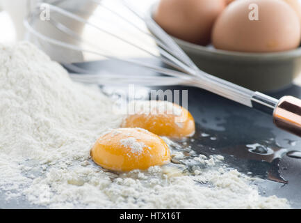 zwei Knickeier zeigen gelbe Dotter auf einen Haufen von weißes Mehl mit einem Schneebesen und vollen Eiern in den Boden zurück, schoss mit Schwerpunkt Thema Stockfoto