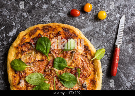 Hausgemachte Pizza mit Käse, Schinken, Salami, Babyspinat und Shimeji Pilze. Frisch gebackenes italienisches Essen fertig zum Verzehr. Stockfoto