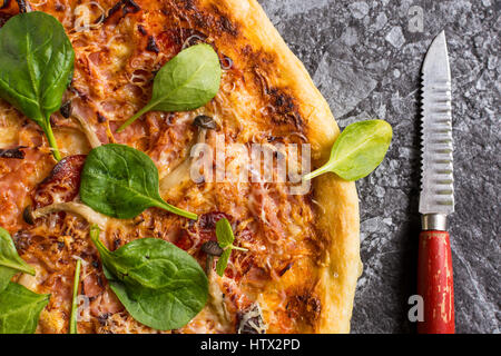 Hausgemachte Pizza mit Käse, Schinken, Salami, Babyspinat und Shimeji Pilze. Frisch gebackenes italienisches Essen fertig zum Verzehr. Stockfoto