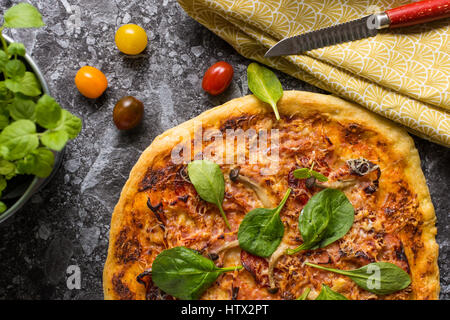 Hausgemachte Pizza mit Käse, Schinken, Salami, Babyspinat und Shimeji Pilze. Frisch gebackenes italienisches Essen fertig zum Verzehr. Stockfoto