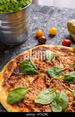 Hausgemachte Pizza mit Käse, Schinken, Salami, Babyspinat und Shimeji Pilze. Frisch gebackenes italienisches Essen fertig zum Verzehr. Stockfoto