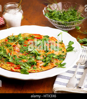 Gemüse Omelett mit Erbsen schießt Microgreens auf weißer Teller, Vintage Holztisch, Silber Gabel und Messer Stockfoto
