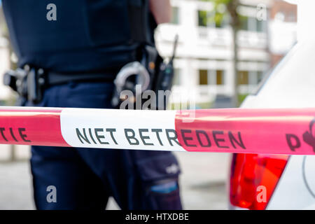Niederländische Polizei Linie nicht überqueren. Roter Kunststoff Klebeband und Polizist, Pistole Gürtel, Handschellen und Waffe am Tatort eines Verbrechens. Stockfoto