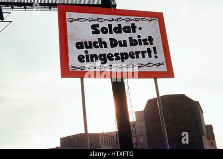 Roten und weißen Schild mit Stacheldraht Grafik an der Grenze zwischen West-Berlin und Ost-Berlin, während des Kalten Krieges, mit Text auf Deutsch lesen "Soldat Auch du Bist Eingesperrt" oder "Soldaten Sie auch gefangen sind", Förderung der ostdeutschen Soldaten in den Westen, Deutschland, 1975 defekt. Stockfoto