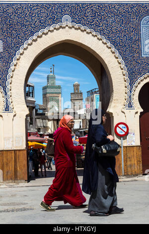 Fes, Marokko.  Zwei Frauen mittleren Alters gehen vorbei an der Bab Boujeloud, Eingang zum Fes El-Bali, der alten Stadt.  Das Minarett der Medersa Bou Inania ist in Stockfoto