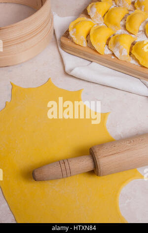 Nahaufnahme von mehreren fertig zum Kochen von Wareniki, Teigtaschen, Piroggen mit Hüttenkäse oder Quark auf Holzbrett mit Mehl. Frisch zubereitet Stockfoto
