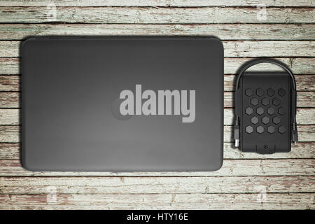 Schwarzer Laptop mit dem geschlossenen Deckel und eine externe Festplatte liegen auf einem Holztisch von der alten leichten Boards. Stockfoto