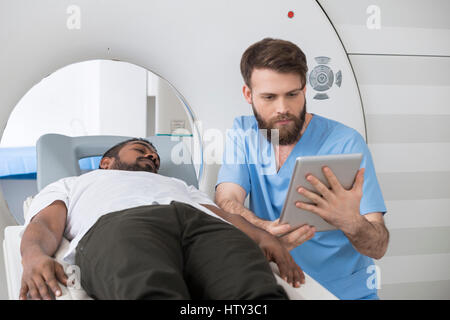 Arzt mit Digital-Tablette von Patienten liegen auf CT-Scanner Stockfoto