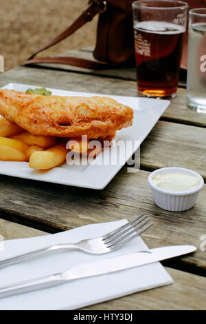 Fish And Chips, englische Traditionsgericht auf eine Kneipe im freien Holztisch, Bier auf dem Hintergrund Stockfoto