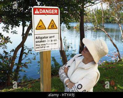 Miami, Florida, Frau liest Zeichen Warnung vor Gefahr, Alligatoren und Schlangen neben Lagune. Stockfoto