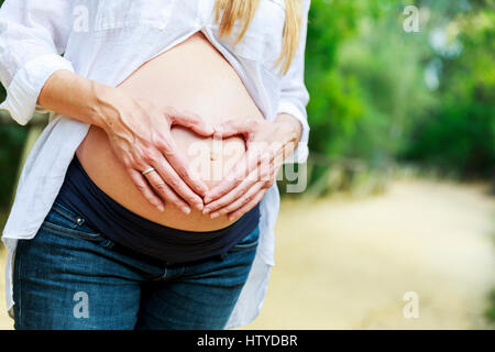 Frau macht Herzform mit ihr die Hände auf ihren schwangeren Bauch Stockfoto