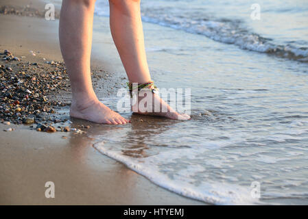 Frauenbeine stehen am Rand des Wassers am Strand Stockfoto