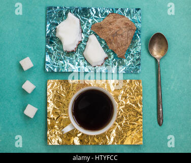 Stücke der Kokosnuss und eine Tasse Kaffee auf steht aus gelb und Türkis Folie auf einer Holzoberfläche Stockfoto