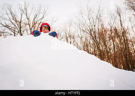 Junge spielt auf einem Schneehaufen Stockfoto