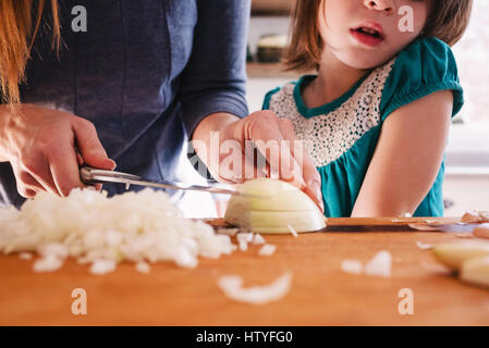 Mutter Unterricht ihrer Tochter Zwiebeln hacken Stockfoto