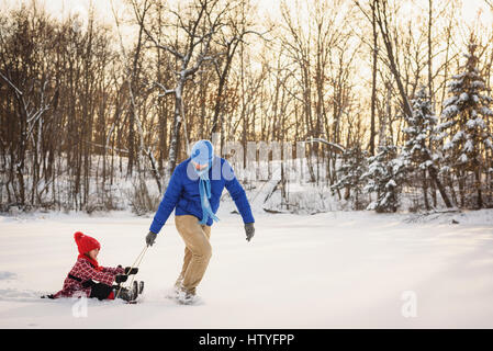 Vater Tochter auf einem Schlitten in den Schnee ziehen Stockfoto