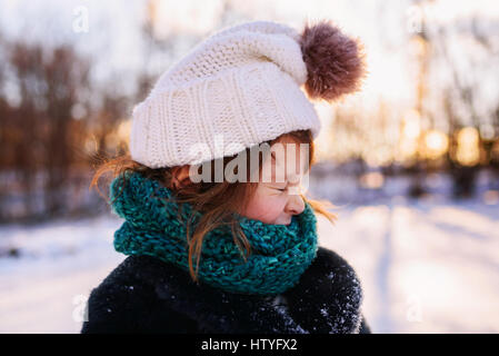 Mädchen in Pudelmütze und Schal im Schnee ziehen ein lustiges Gesicht stehen Stockfoto