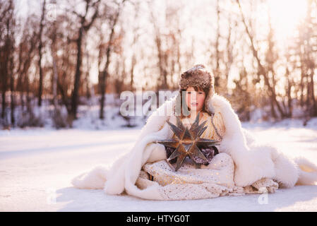 Mädchen, verkleidet als Schneekönigin sitzen im Schnee Stockfoto