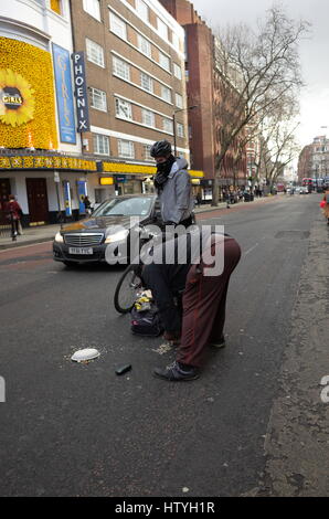 Obdachloser holt sein Geld von der Straße, nachdem er bei einem Zusammenstoß mit einem Radfahrer in London, England Stockfoto