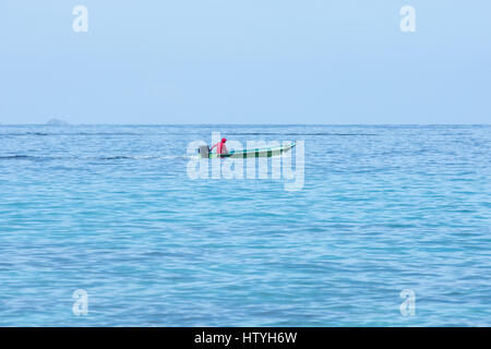 Mann in einem kleinen Boot mit Außenbordmotor Segel Geschwindigkeiten über die Szene einer ruhigen blauen Meer und strahlend blauen Himmel. Stockfoto