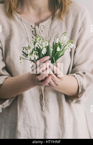 Bouquet von wilden Schneeglöckchen in weiblichen Händen. Frau in weißem Leinen Kleid. Tageslicht. Frühling Geschenk. Stockfoto