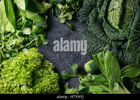 Vielzahl von rohem Gemüse Salate, Salat, Chinakohl, Mais, Brokkoli, Wirsing als Frame über schwarze Steinstruktur Hintergrund. Ansicht von oben, Raum Stockfoto