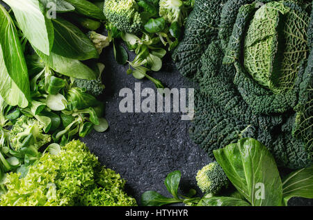 Vielzahl von rohem Gemüse Salate, Salat, Chinakohl, Mais, Brokkoli, Wirsing als Frame über schwarze Steinstruktur Hintergrund. Ansicht von oben, Raum Stockfoto