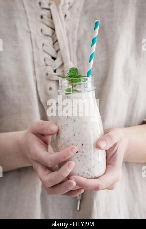 Eine Flasche Smoothie mit Chia-Samen, Heidelbeeren, Minze und retro gestreiftes cocktail Rohr in weiblichen Händen. Frau in weißem Leinen Kleid. Gesunde eati Stockfoto