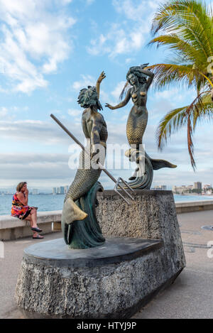 Skulptur von Triton und Meerjungfrau von Carlos Espino (Neptun und die Nereide) auf Puerto Vallarta Malecon w / Frau im Hintergrund mit bunten Kleid Stockfoto