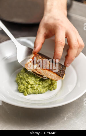 Koch dient gegrillten Lachs über ein Korn des grünen Risottoreis Stockfoto