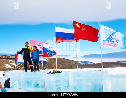 SAHYURTA, Gebiet IRKUTSK, Russland - März 11.2017: Cup des Baikalsees. Winter-Schwimmwettkampf. Russe und chinesische Frau auf einen Eiswürfel direkt neben Kirche St. Stockfoto
