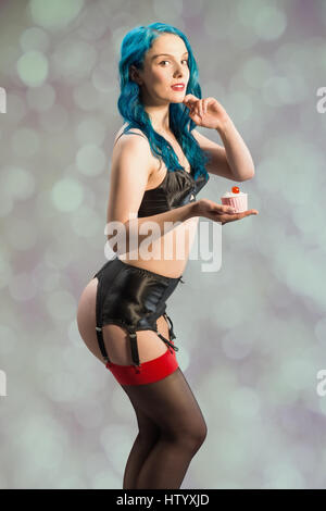 Freche Pin up Mädchen mit blauen Haaren hält einen Cupcake mit Kirsche obenauf Stockfoto