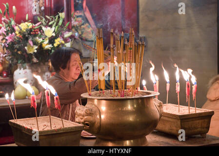 Eine lokale Frau an den Man Mo Tempel in Hong Kong Beleuchtung Weihrauch hält vor dem Gebet. Stockfoto