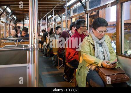 Passagiere sitzen in einer Straßenbahn Fahrt entlang einer Straße in Causeway Bay mit einer Frau, die ihr Handy überprüfen. Stockfoto