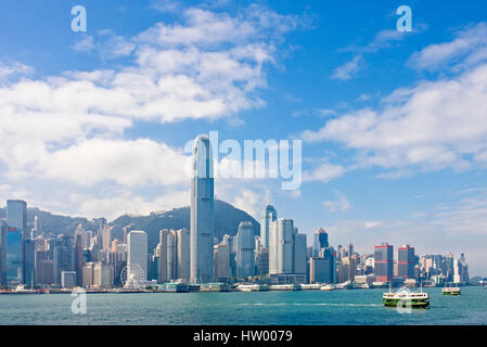 Ein Stadtbild Ansicht der Gebäude entlang Hong Kong Island mit einem Star Ferry im Vordergrund an einem sonnigen Tag mit blauem Himmel. Stockfoto