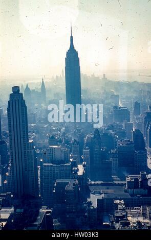 Panorama mit Blick auf südlich der Innenstadt von Skyline von Manhattan in New York City, 1957. Im Zentrum steht das Empire State Building, das Hotel liegt an der Fifth Avenue und 34th Street. Links im Vordergrund ist 500 Fifth Avenue, gelegen an der 42nd Street in Midtown. Im Hintergrund sind der Metropolitan Life Insurance Company Tower und andere untere Manhattan Wolkenkratzer in der Mittagssonne Silhouette. Die Freiheitsstatue ist im Dunst im Hafen ersichtlich. Stockfoto