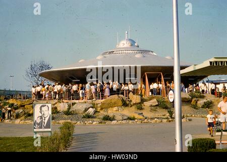 Blick auf Besucher warten auf Linie außerhalb der Braniff Airways Raumschiff fliegende Untertasse Attraktion in der Satellitenstadt Ausstellung im Freedomland USA Themenpark, befindet sich im Abschnitt Baychester aus der Bronx, New York City, September 1961. Ein Zeichen in der unteren linken Vordergrund sichtbar wirbt kommende Harry James Orchestra-Aufführungen auf dem Mond Bowl vom 29. September bis 1. Oktober 1961. Stockfoto