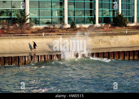 Ein einsamer individuelle Spaziergänge an einem See an der Wand unter Belagerung durch hohe Wellen in Chicago Burnham Hafen. Chicago, Illinois, USA. Stockfoto