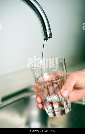 Closeup von einem kaukasischen Jüngling füllt ein Glas mit Wasser aus einem Hahn mit einem kleinen Strom des Wassers Stockfoto