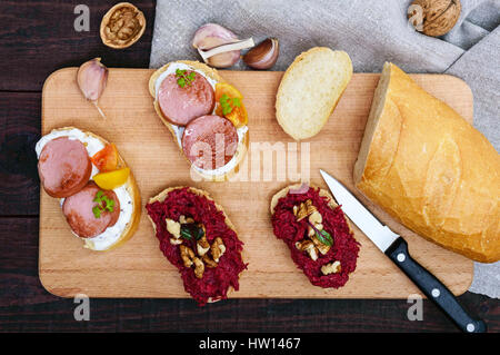 Zwei Arten von Frühstück Sandwiches: mit gegrillten Würstchen und gelbe Tomaten und gekochte geriebene Rüben und Walnüsse. Die Ansicht von oben Stockfoto