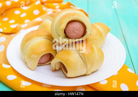 Frisch gebackene kleine Brötchen auf einem weißen Teller. Würstchen im Teig. Stockfoto