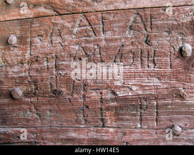 Graffiti, Inschrift auf Holztür. Worte, geschnitzt in eine hölzerne Kapelle Tür mit rostigen metallische Verzierungen (Frankreich) Stockfoto