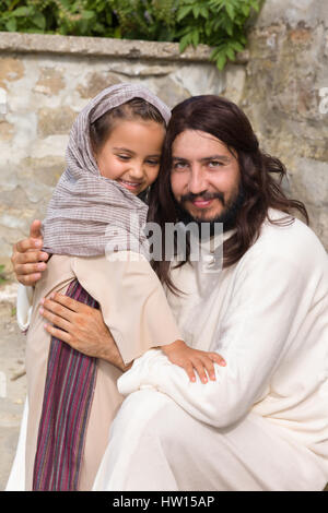 Biblische Szene, in der Jesus sagt: Lasst die Kinder kommen zu mir, ein kleines Mädchen Segen. Historisches Reenactment an einem alten Brunnen. Stockfoto