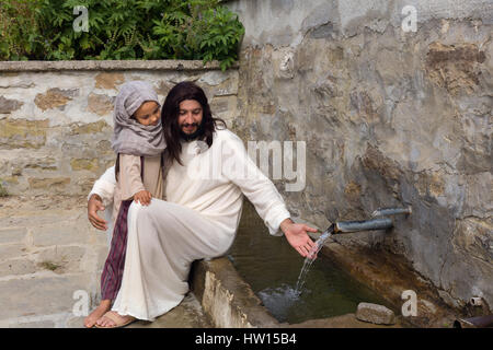 Biblische Szene, in der Jesus sagt: Lasst die Kinder kommen zu mir, ein kleines Mädchen Segen. Historisches Reenactment an einem alten Brunnen. Stockfoto