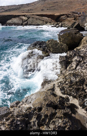 Das azurblaue Wasser des karibischen Meeres Absturzes auf North Shore von Aruba mit der eingestürzten Naturbrücke im Hintergrund. Stockfoto