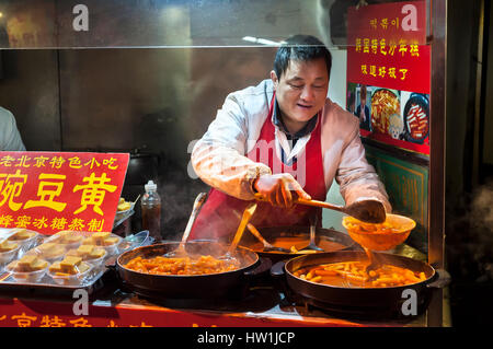 WANGFUJING NIGHT MARKET, Peking - Dec 25, 2013 - den Hersteller würzigen Koreanischen Reis Kuchen an der Wangfujing Snack Street, Beijing. Stockfoto