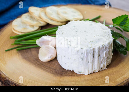 Gewürzte cremige Weichkäse mit Knoblauch und feinen Kräutern auf einer Holzplatte mit Crackern. Stockfoto