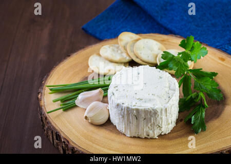 Gewürzte cremige Weichkäse mit Knoblauch und feinen Kräutern auf einer Holzplatte mit Crackern. Stockfoto