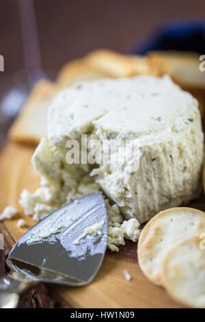 Gewürzte cremige Weichkäse mit Knoblauch und feinen Kräutern auf einer Holzplatte mit Crackern. Stockfoto